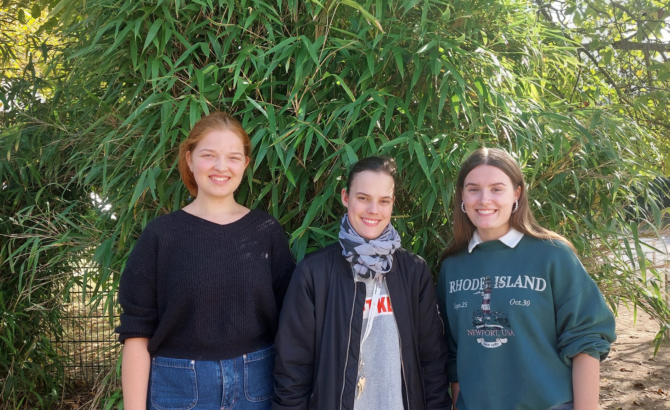 Drei junge Frauen stehen vor einem Bambus und lächeln in die Kamera