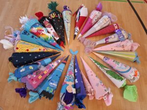 22 bunte, unterschiedliche Schultüten liegen auf dem Turnhallenboden und bilden einen Kreis. Vereinzelt sind Namen zu erkennen.
